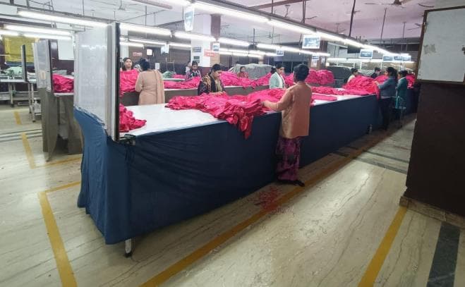 Garment workers handling bright fabric pieces around a production table
